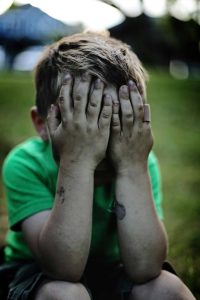 Bambino con volto coperto dalle mani sporche, simbolo di dolore e fragilità infantile