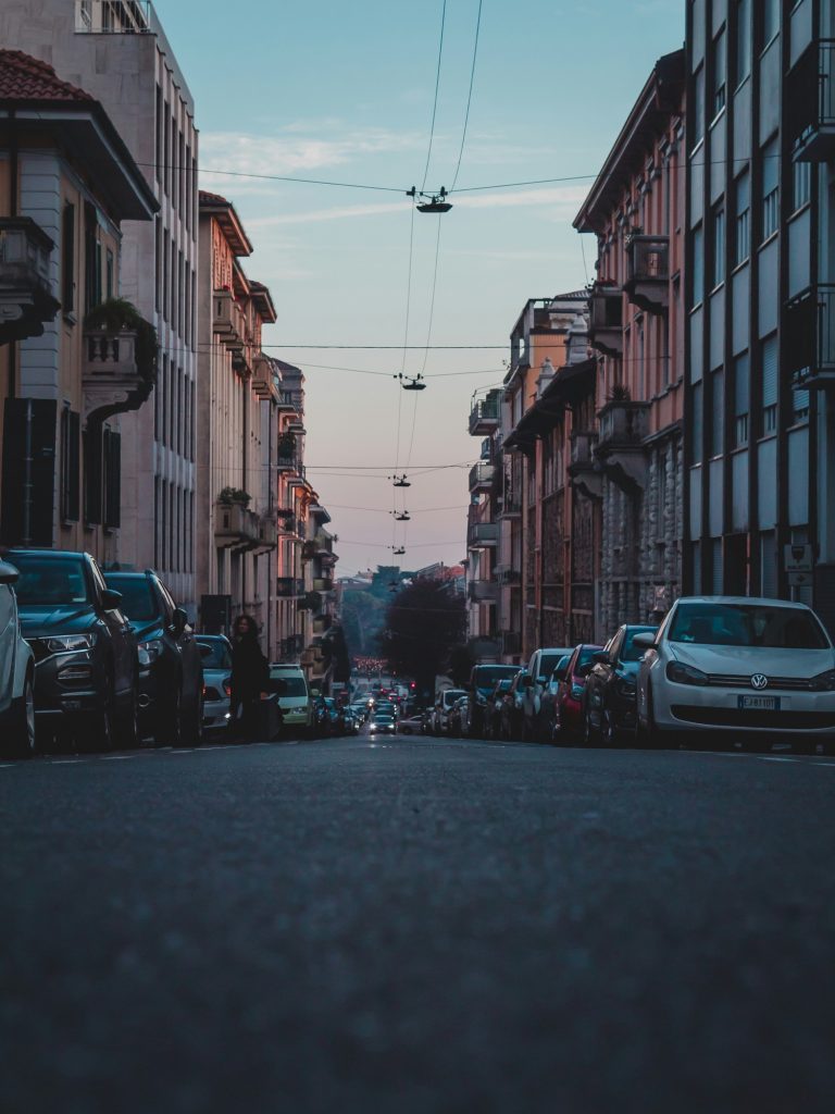 veduta di una strada di Milano al tramonto con auto parcheggiate e palazzi ai lati